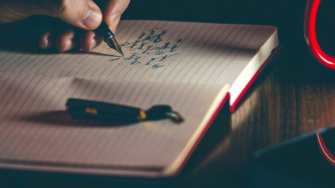 Close-up of hands writing in a notebook with a pen